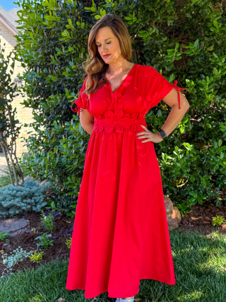 Bright red midi dress with floral applique waist and tie sleeves shown in angled view highlighting flattering fit and flowy silhouette