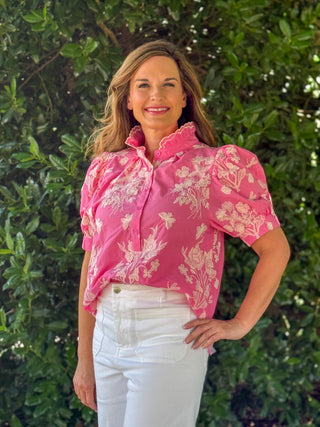 Front view of a pink embroidered top with floral and dragonfly motifs, button-front detail, scalloped neckline, and puff sleeves paired with white jeans.