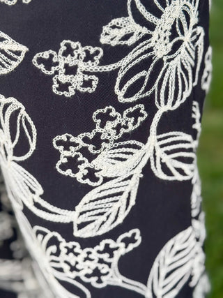 Detailed close-up of ivory floral embroidery on black fabric, showcasing intricate stitching and textured botanical design.