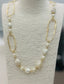 Long gold necklace with pearl beads, neutral stones, and abstract gold links displayed on a boutique jewelry stand