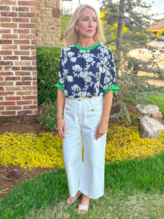 Navy floral embroidered top with green ruffle trim paired with ivory high waisted wide leg culottes and neutral sandals, chic boutique spring outfit