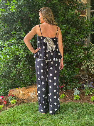 Back view of women's black and white polka dot two-piece outfit featuring adjustable spaghetti straps, striped bow tie back detail, peplum top, and flowy wide leg pants.