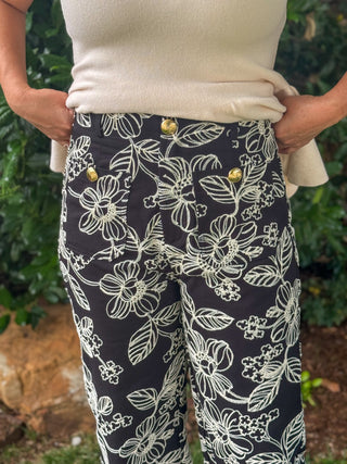 Close-up of black embroidered pants featuring ivory floral stitching, decorative gold buttons, and tailored front pocket details.
