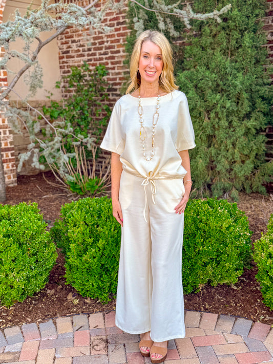 Cream knit short sleeve top with drawstring waist paired with matching wide leg pants, chic neutral boutique lounge set styled with sandals and layered necklace