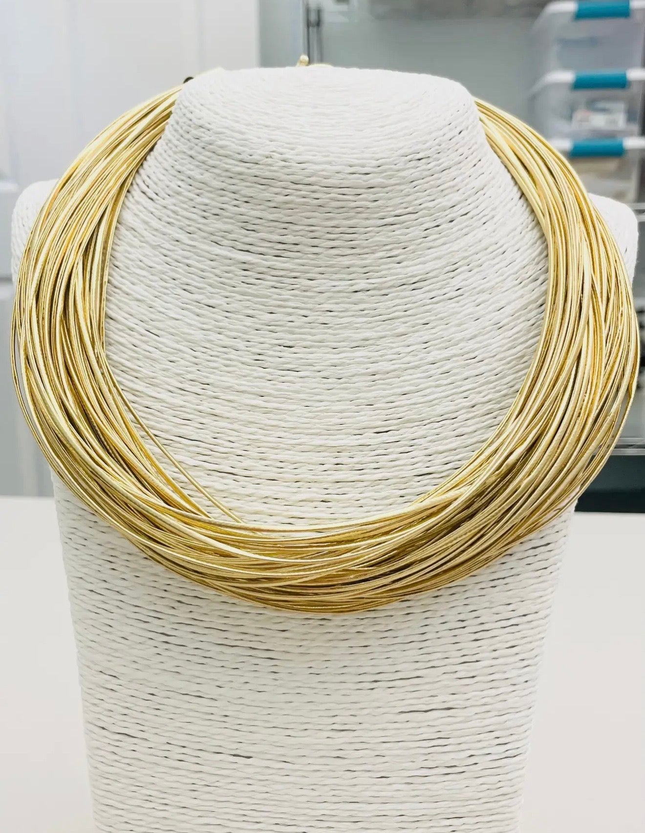 Layered gold collar statement necklace with multiple sleek strands and oversized clasp displayed on boutique jewelry stand