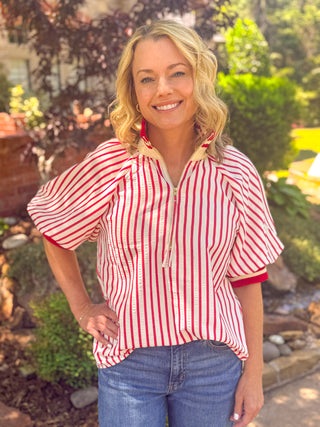 Woman wearing a red and white striped puff sleeve half-zip top with contrast ribbed trim styled with blue jeans outdoors.

