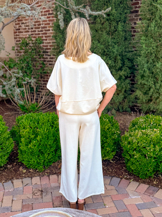 Cream knit short sleeve top with drawstring waist paired with matching wide leg pants, chic neutral boutique lounge set styled with sandals and layered necklace