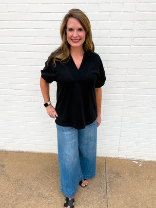 Women’s black V-neck top with short puff sleeves and relaxed fit styled with wide-leg jeans