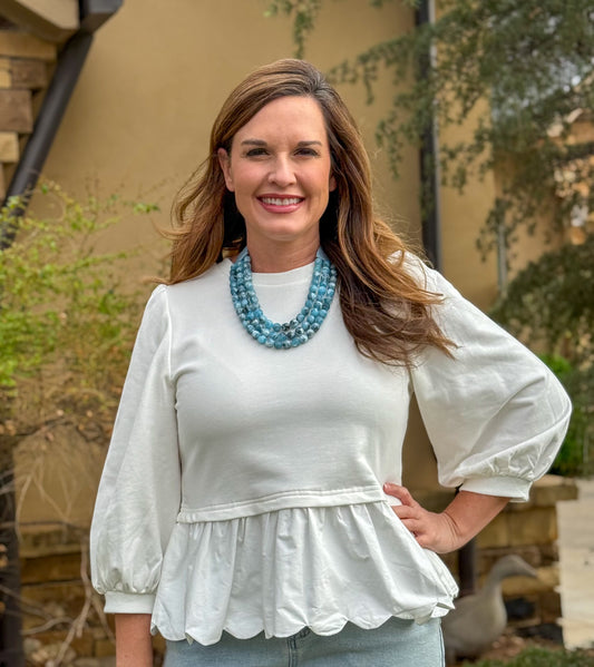 White peplum blouse with long puff sleeves styled with light wash denim and blue statement necklace for women’s boutique fashion
