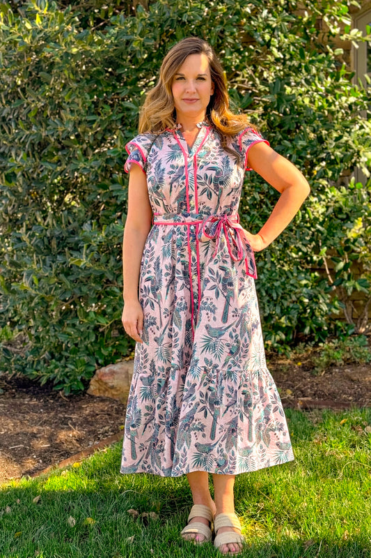 Pink tropical print midi dress with contrast trim, short flutter sleeves, and tie waist belt styled for spring and summer boutique fashion