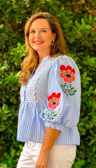 Close up of blue striped blouse with red floral embroidery on puff sleeves, lightweight boutique top with textured detail and feminine fit