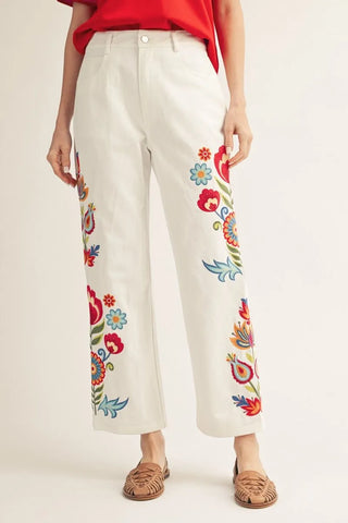 Wildflower Lane embroidered ivory cotton pants with colorful floral embroidery, high-rise waist, straight-leg fit, pockets, and button front closure.